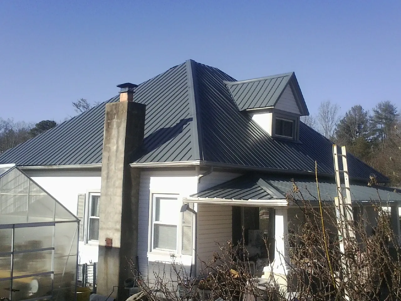 Dark blue standing seam metal roof on a white farmhouse with dormer — Slate & Tile Roof Repair by Roofing Brothers in Lucile