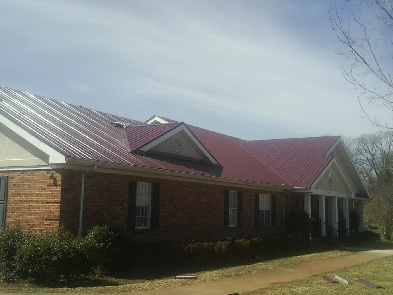 Red metal roof with gabled entries on a long brick building, from a Hail Damage Roof Repair job in Lucile