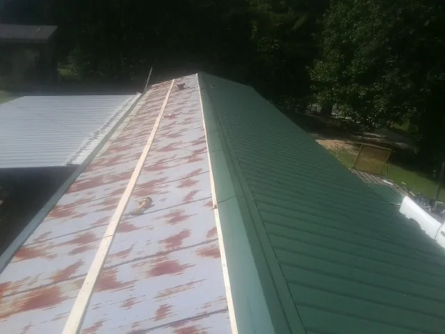 Old rusted panels beside newly installed green metal roofing — Wind Damage Roof Repair by Roofing Brothers in Lucile