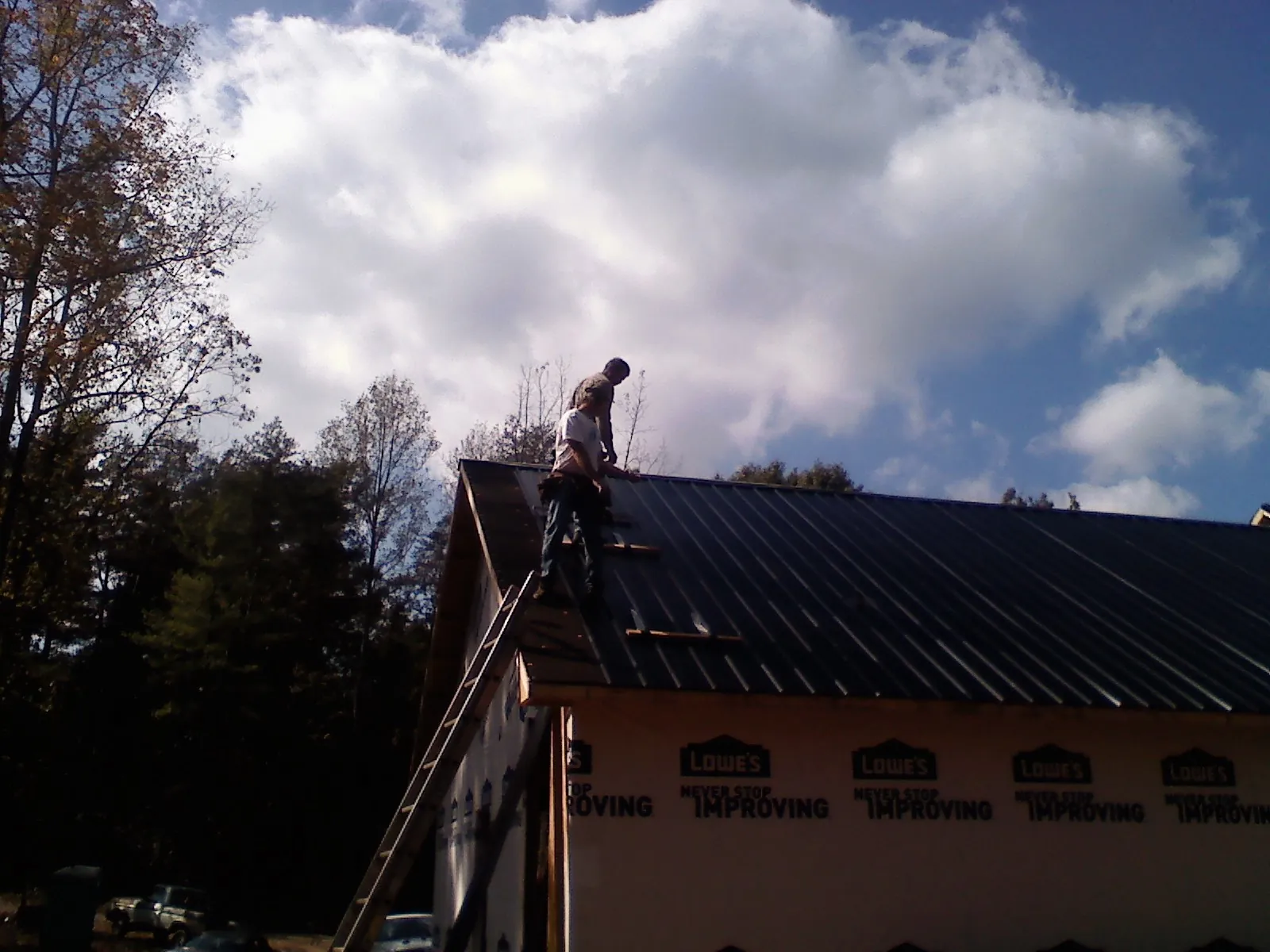 Roofer fastening dark metal panels high against a cloudy sky, from a Roof Inspection job in Lucile