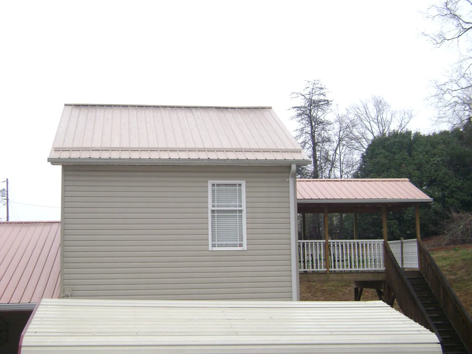 Tan metal roofs on a two story addition and attached porch, from a Roof Replacement job in Lucile